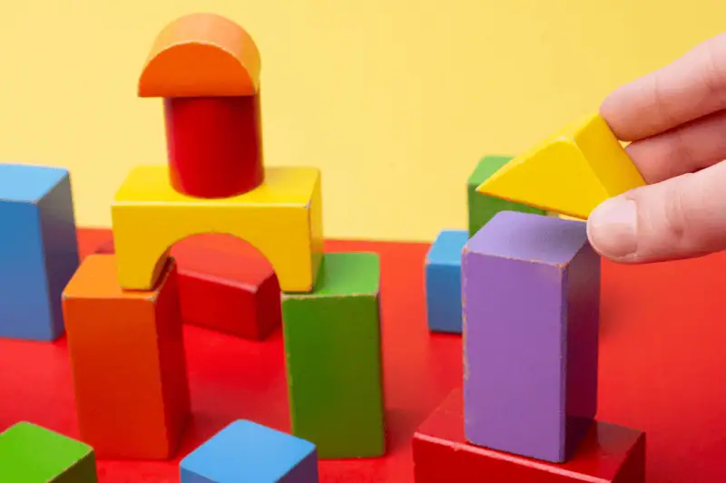 積み木の遊び風景、カラフルなブロックと子供の手が木製のおもちゃを積み重ねるシーン。子供の思考力や創造力を育む教育玩具のイメージ。.